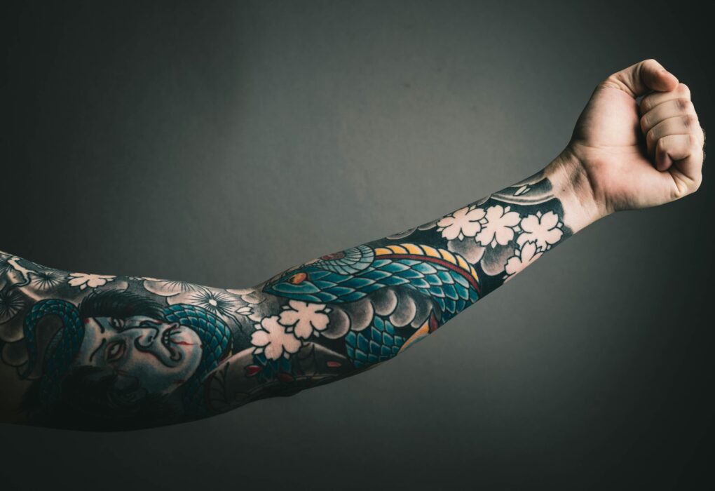 A close-up of a tattooed arm with a colorful sleeve design, featuring floral and artistic elements.